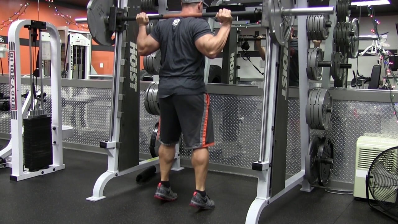 man doing squats on a smith machine in a gym
