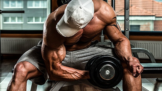 man with white baseball cap doing dumbbell concentration curls