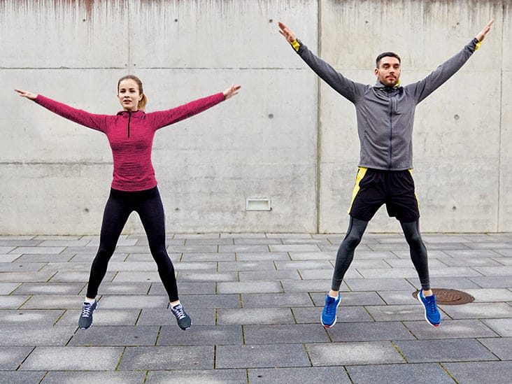 man and woman doing jumping jacks outside