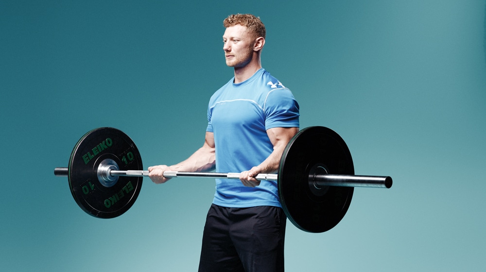 man with red hair wearing a blue shirt doing wide grip barbell curls