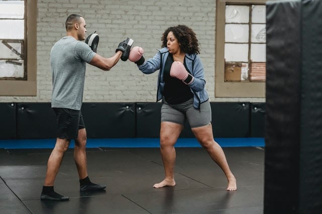 woman using focus mitts with a boxing trainer