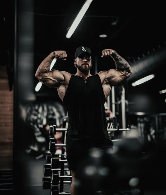 Chris Bumstead Flexing Biceps in Mirror at Gym