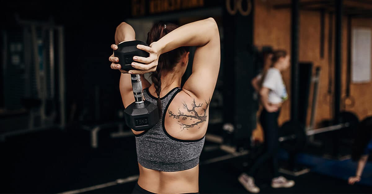 woman in gray sports bra doing a dumbbell tricep overhead extension