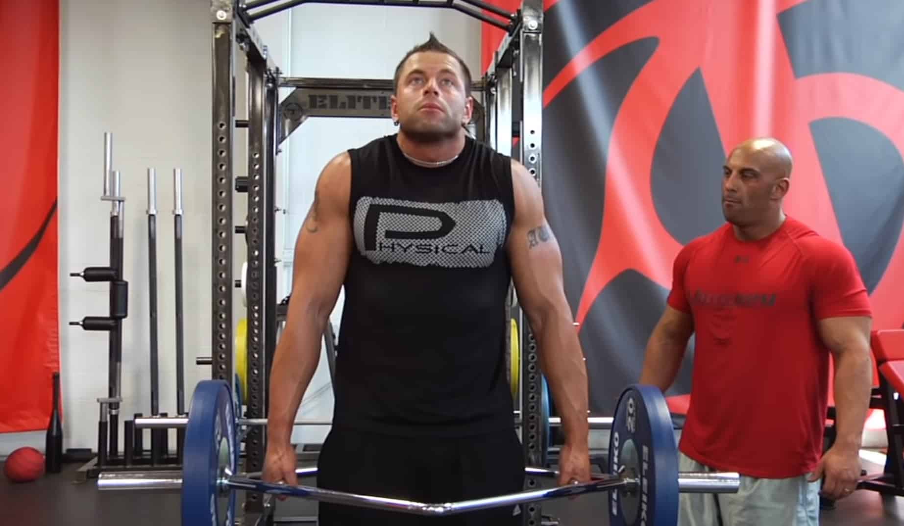 man in black being assisted while doing trap bar shrug