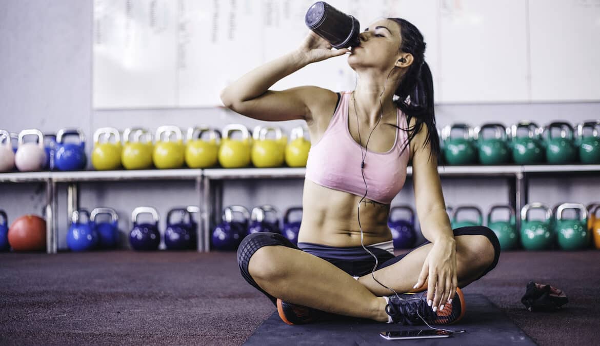 Women Sitting on Gym Mat Drinking a Pre-Workout Drink