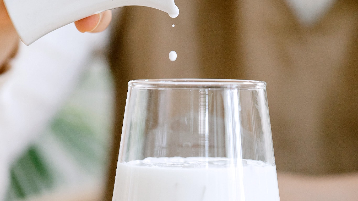 Woman Pouring Milk Into A Glass Cup Woman Pouring Milk Into A Glass Cup